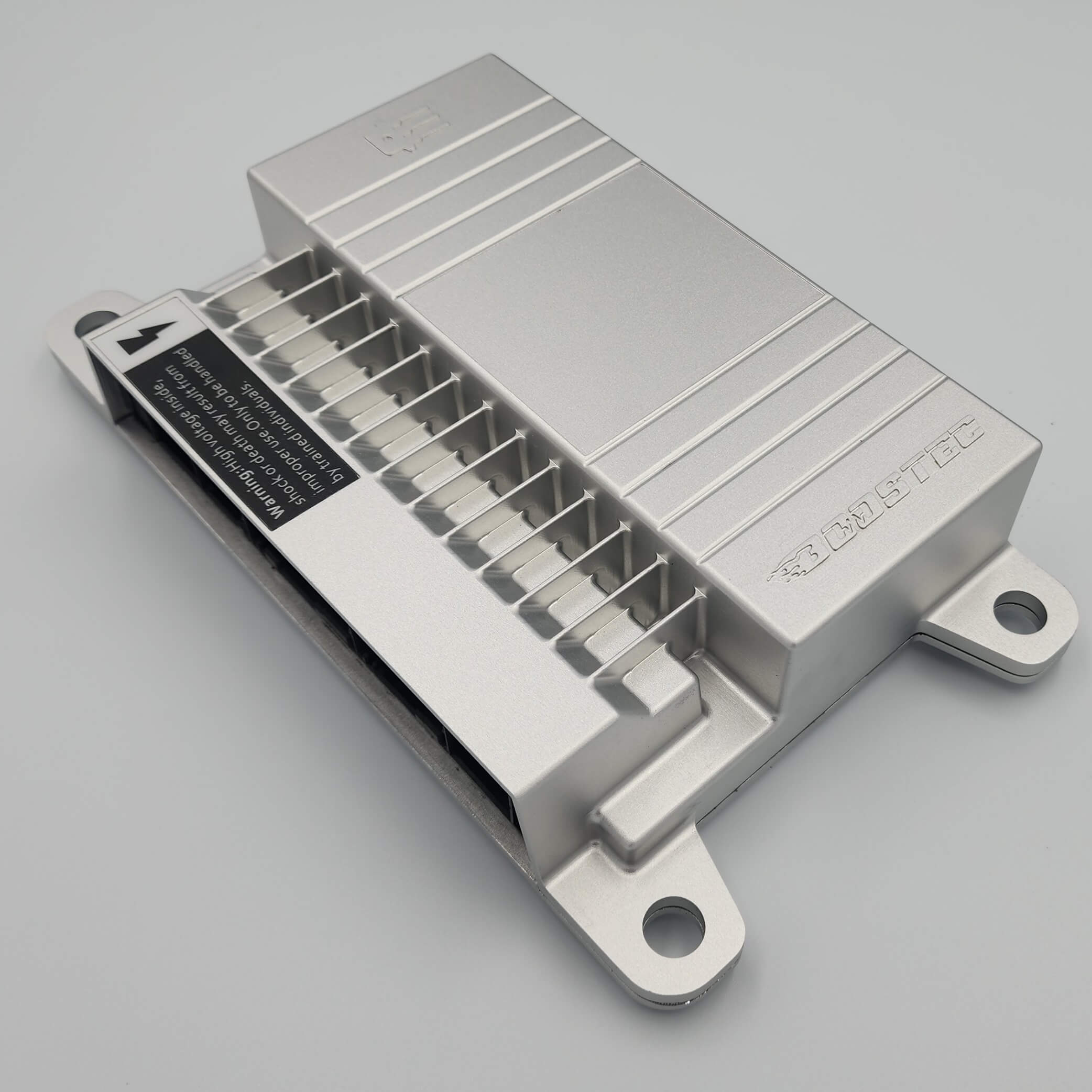 Silver metal component with ribbed fins, brackets, and label on grey.